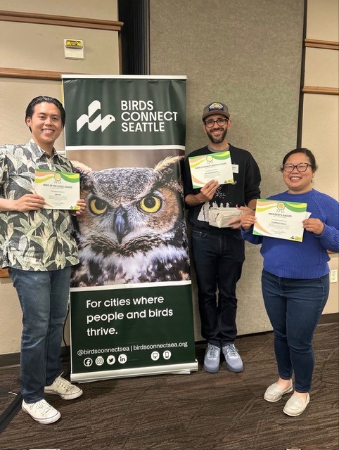 Photo features a Sandhill Crane, a large bird, standing on one leg with wings open.