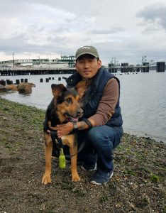 Photo features a man on a beach with a dog.