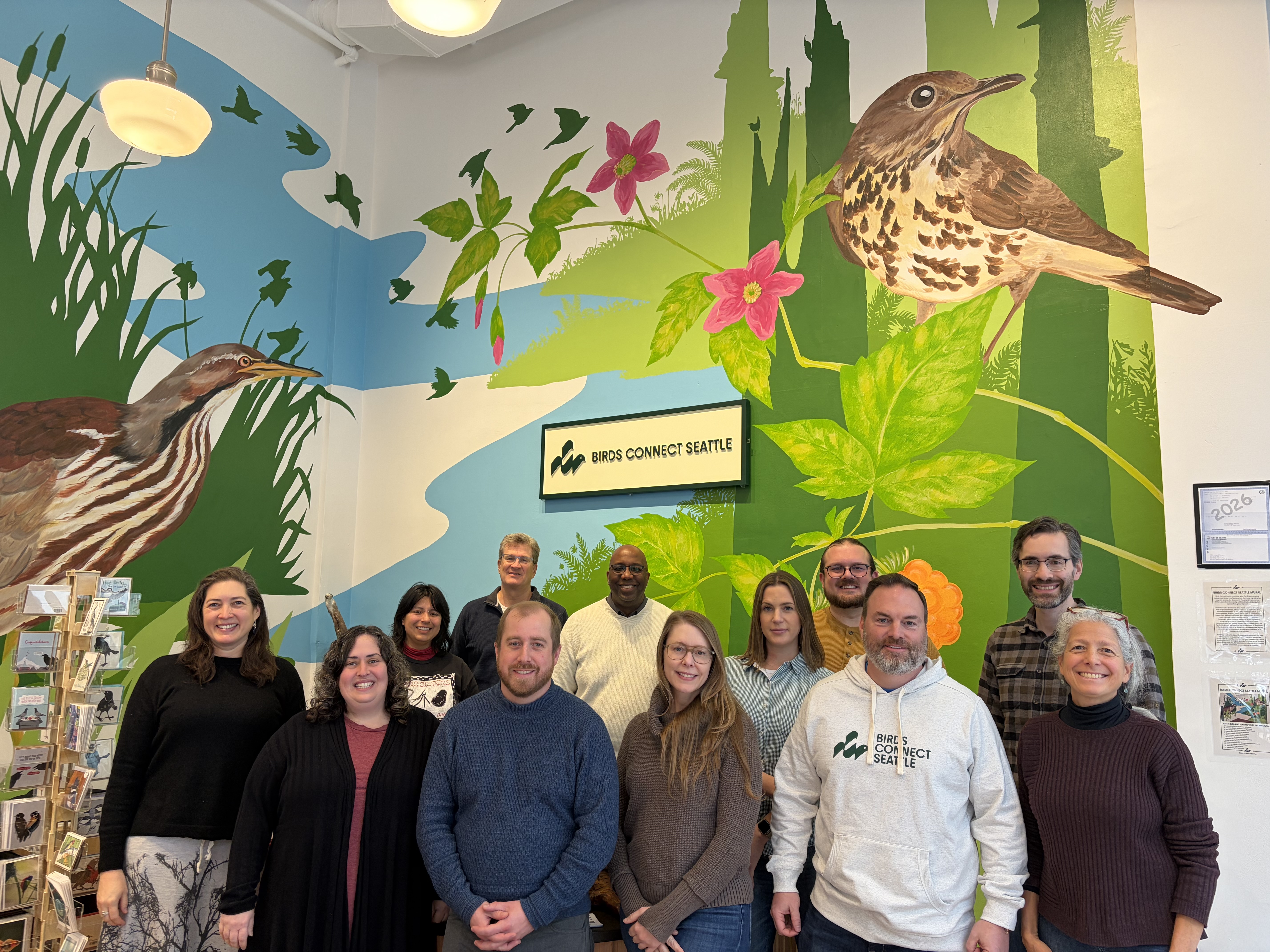 Photo features a Sandhill Crane, a large bird, standing on one leg with wings open.