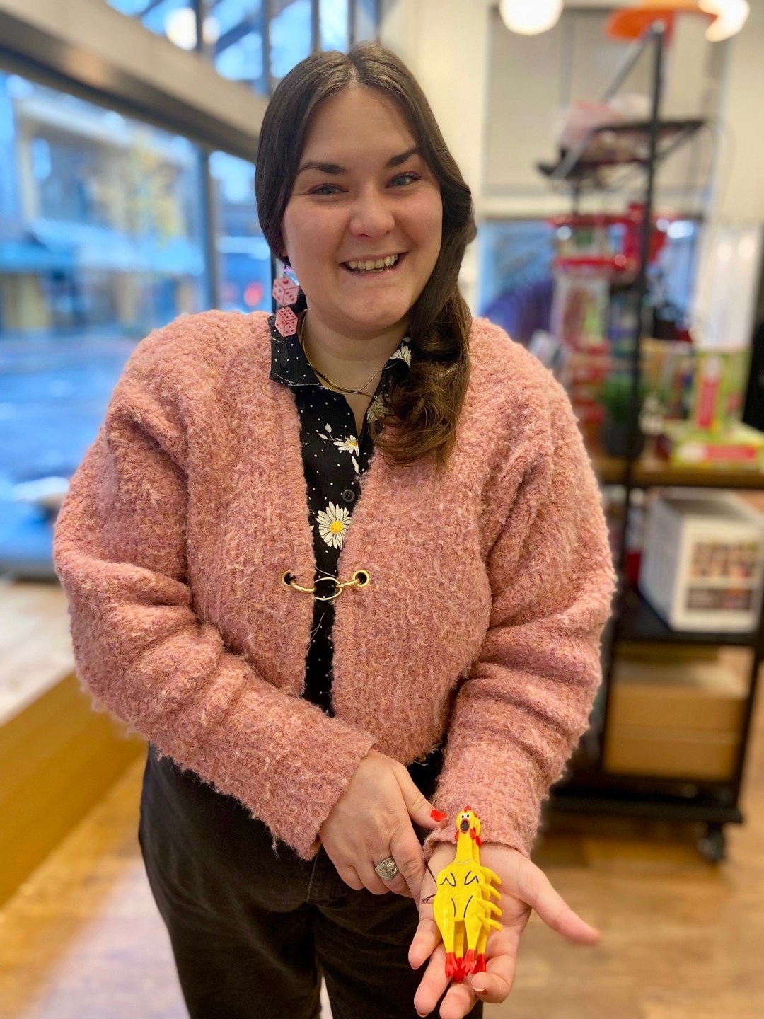 Photo features a person wearing a fluffy pink top and holding a plastic rubber chicken hair clip.