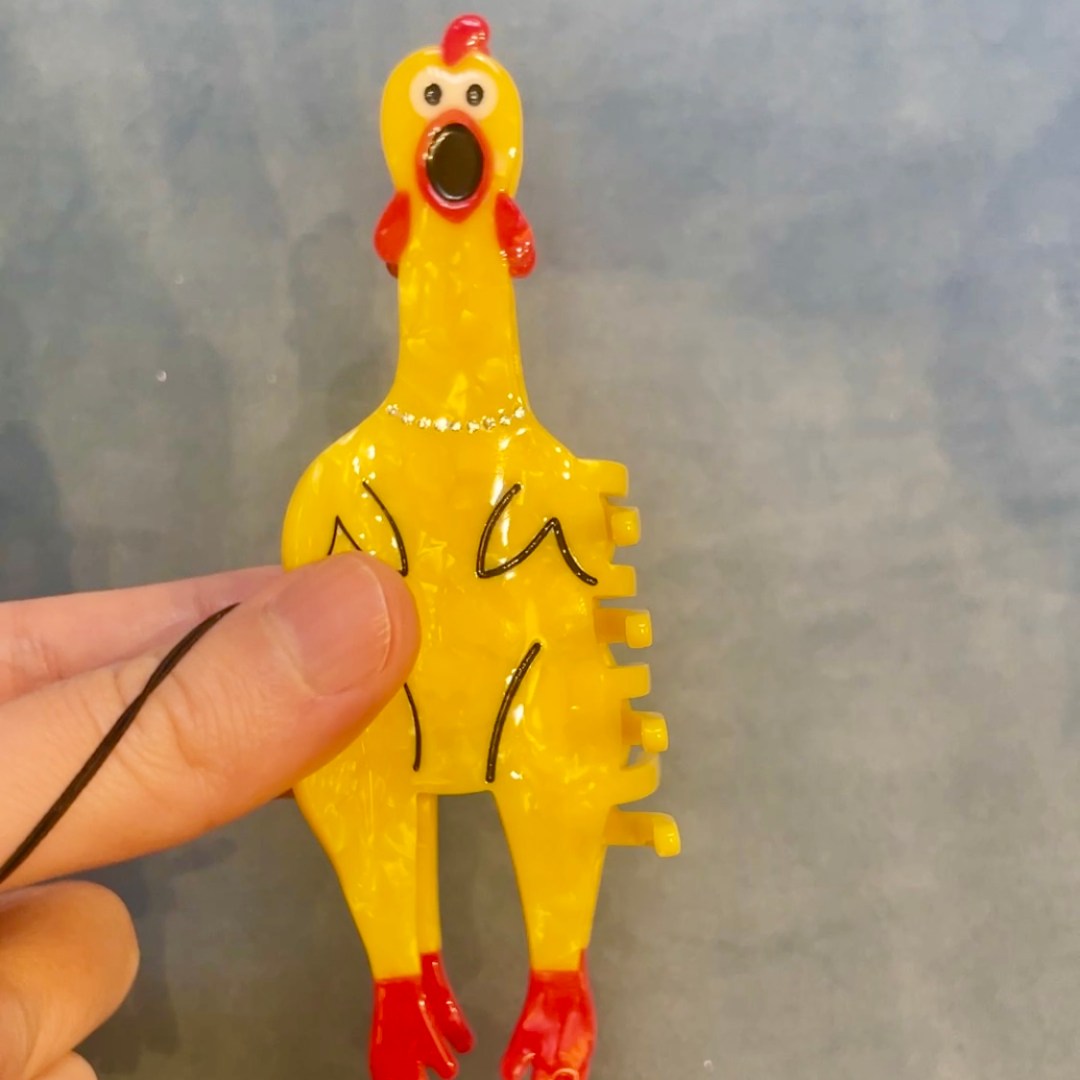 Photo features a yellow plastic rubber chicken hair clip against a blue-gray background.