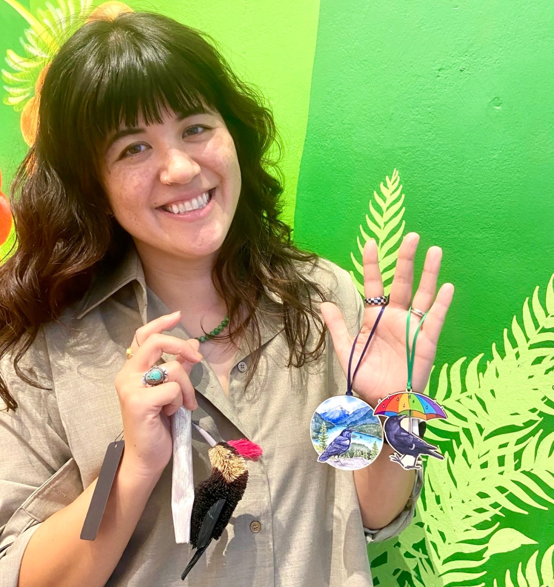 Photo features a woman with long brown hair holding a collection of brightly colored bird ornaments.