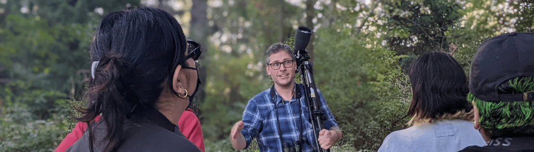 Photo features a Sandhill Crane, a large bird, standing on one leg with wings open.