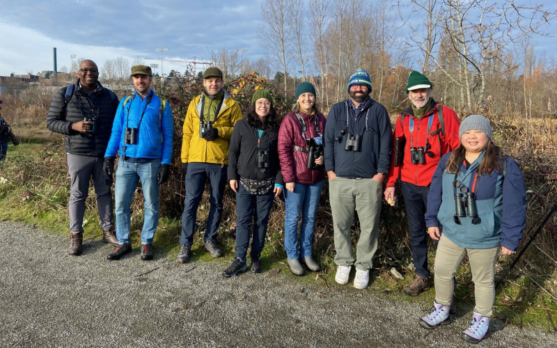 Photo features a Sandhill Crane, a large bird, standing on one leg with wings open.