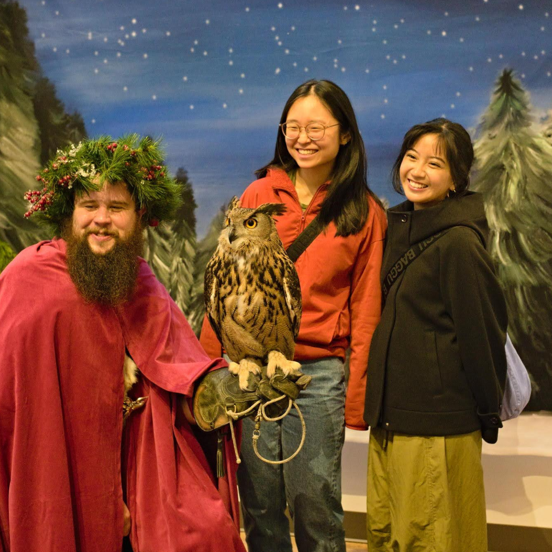 Photo features two women posing with a man holding an owl against a winter backdrop.